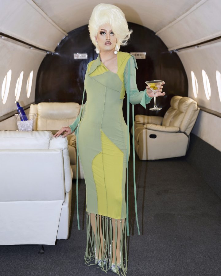 Jesse posing in drag in a priate jet with a martini in hand